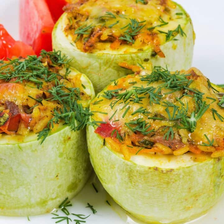 Three stuffed squash on white plate with cut tomatoes in background.