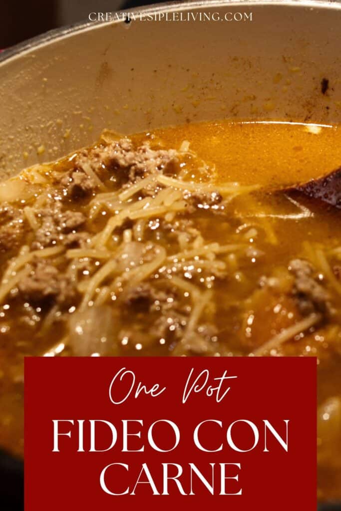 Close-up of a pot filled with fideo con carne soup, showing noodles, ground beef, and broth, with a wooden spoon inside. Text overlay reads “One Pot Fideo Con Carne.”.