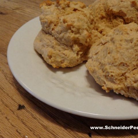 A close-up of three golden brown and crumbly biscuits made from biscuit and pancake mix, resting on a white plate placed on a wooden table.