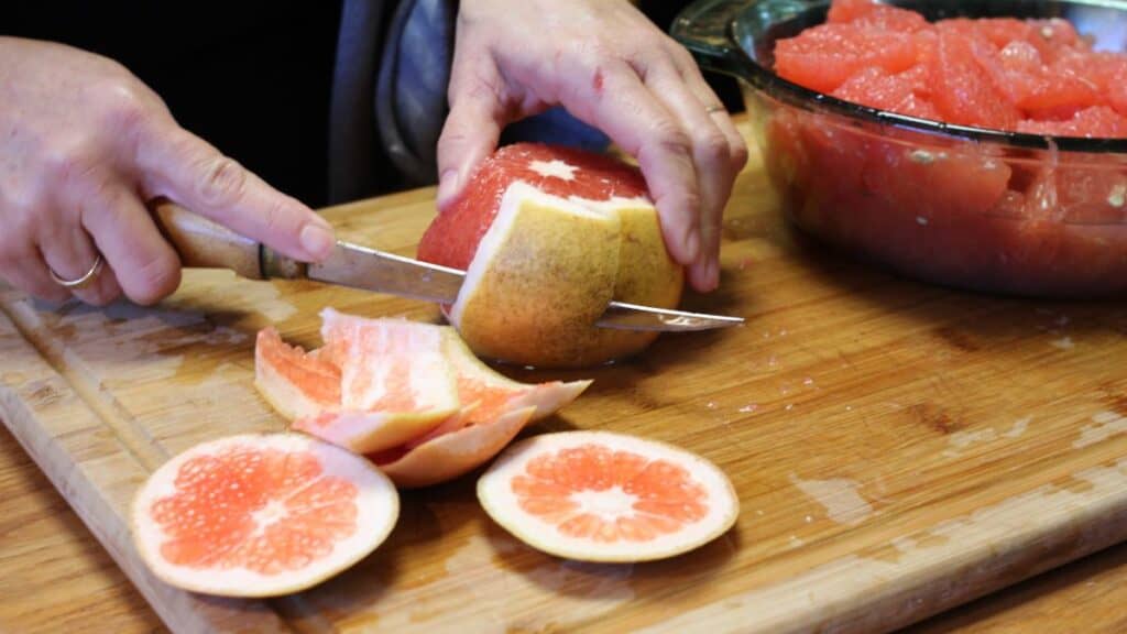 a woman cutting the rind off a grapefruit