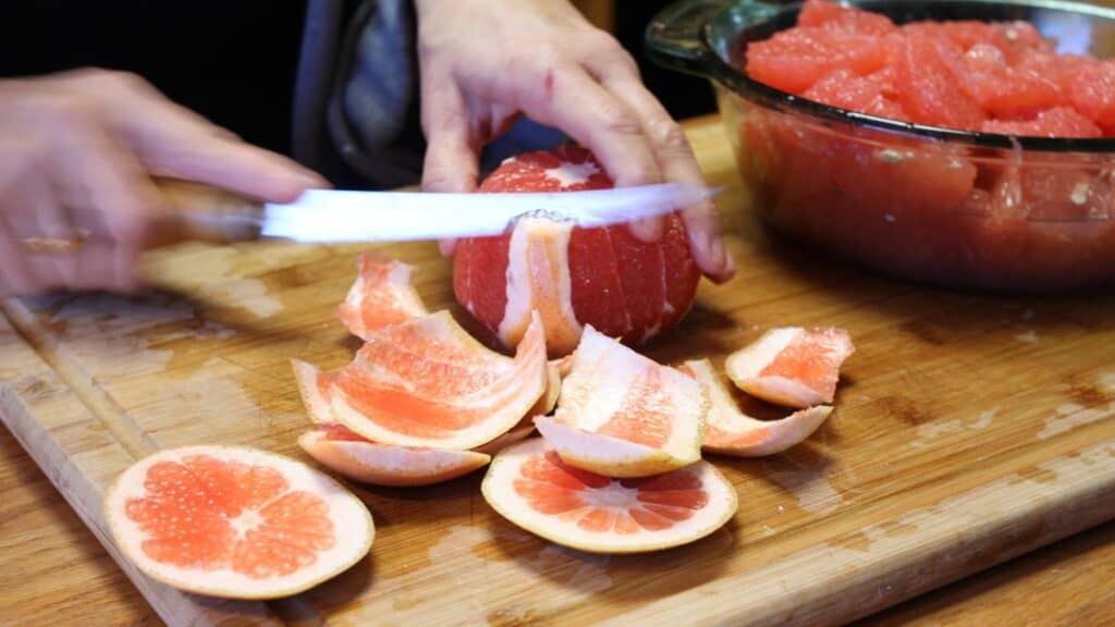a woman cutting the rind off a grapefruit