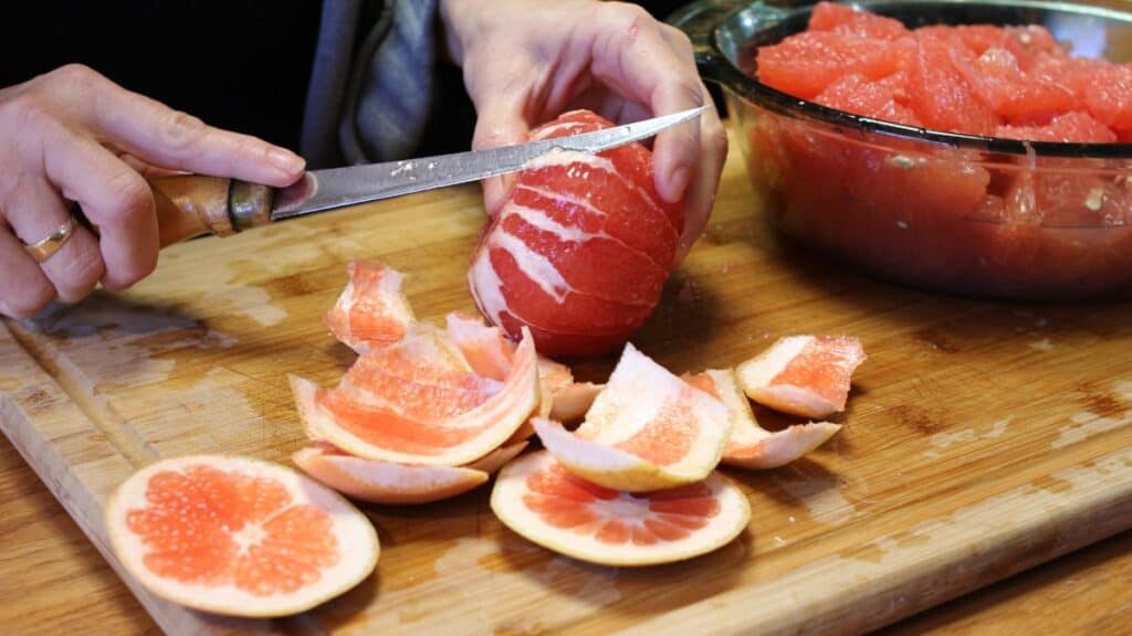 a woman cutting the pith off a grapefruit