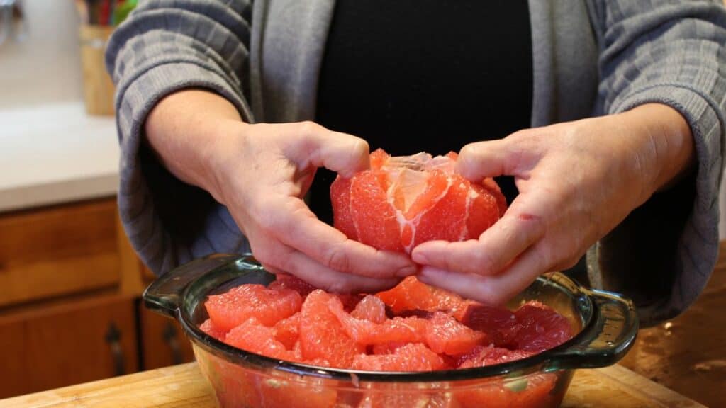 a woman pulling apart a peeled grapefruit
