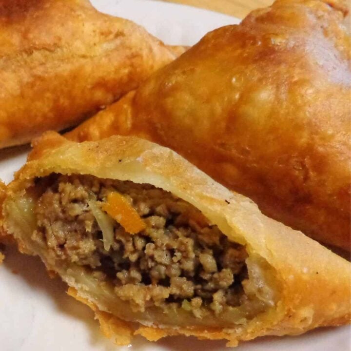 A close-up of a golden-brown Kenyan Samosa, one cut open to reveal a savory filling of minced meat, diced vegetables, and spices, served on a white plate.