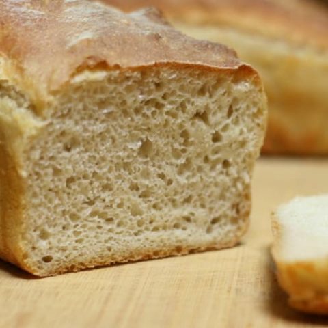 Close-up of a freshly baked loaf of bread with a golden crust on a wooden surface. A slice is cut and placed nearby, revealing the airy texture inside—a testament to timeless homemaking skills.