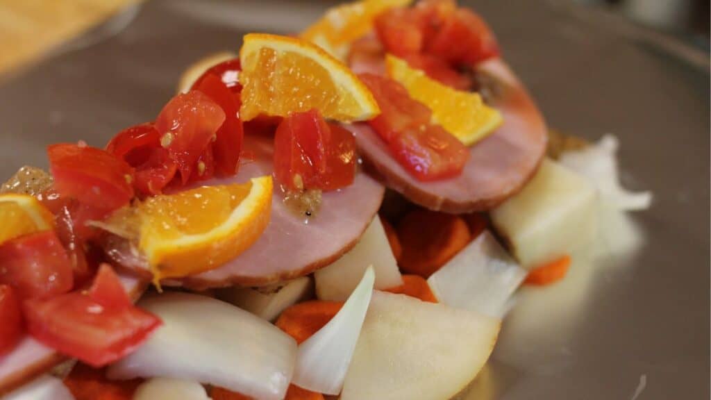 Sliced ham topped with orange wedges and chopped tomatoes on a bed of chopped onions, carrots, and potatoes—perfect for making delicious silver turtles over the campfire.