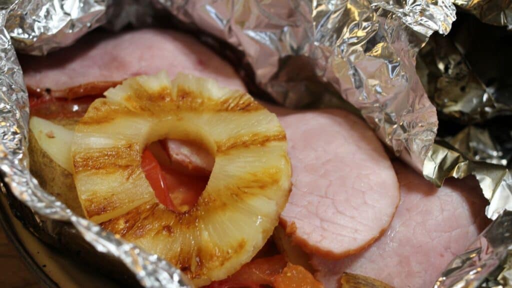 Sliced ham topped with a ring of grilled pineapple, partially wrapped in aluminum foil like classic silver turtles.