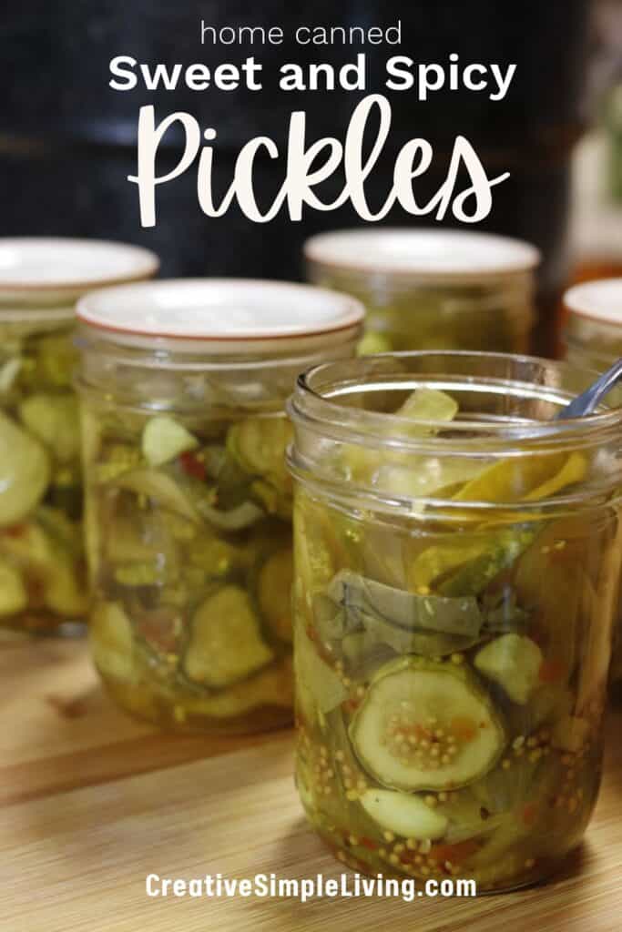 Four glass jars filled with sweet and spicy pickles, with a spoon in the front jar. Text on the image reads “home canned Sweet and Spicy Pickles” and “CreativeSimpleLiving.com.”.