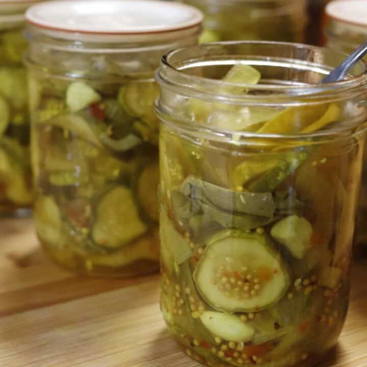 several jars of home canned sweet and spicy pickles. One is open and has a fork in it.