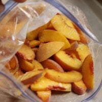 A clear plastic bag filled with sliced peaches, showing the yellow-orange fruit with reddish edges. The bag is partially open, revealing the fruit inside.